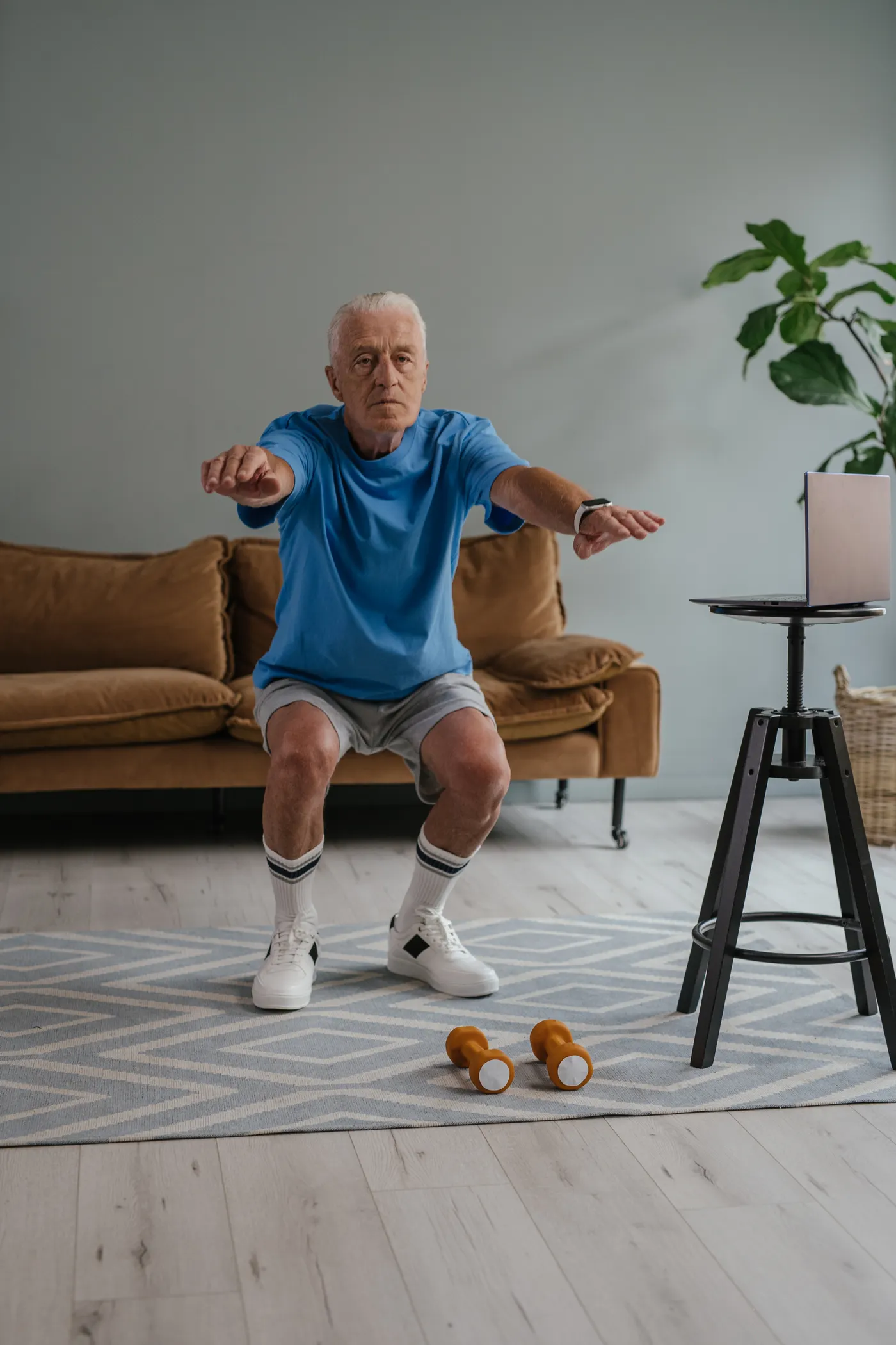 Older man performing a supported dumbbell squat indoors