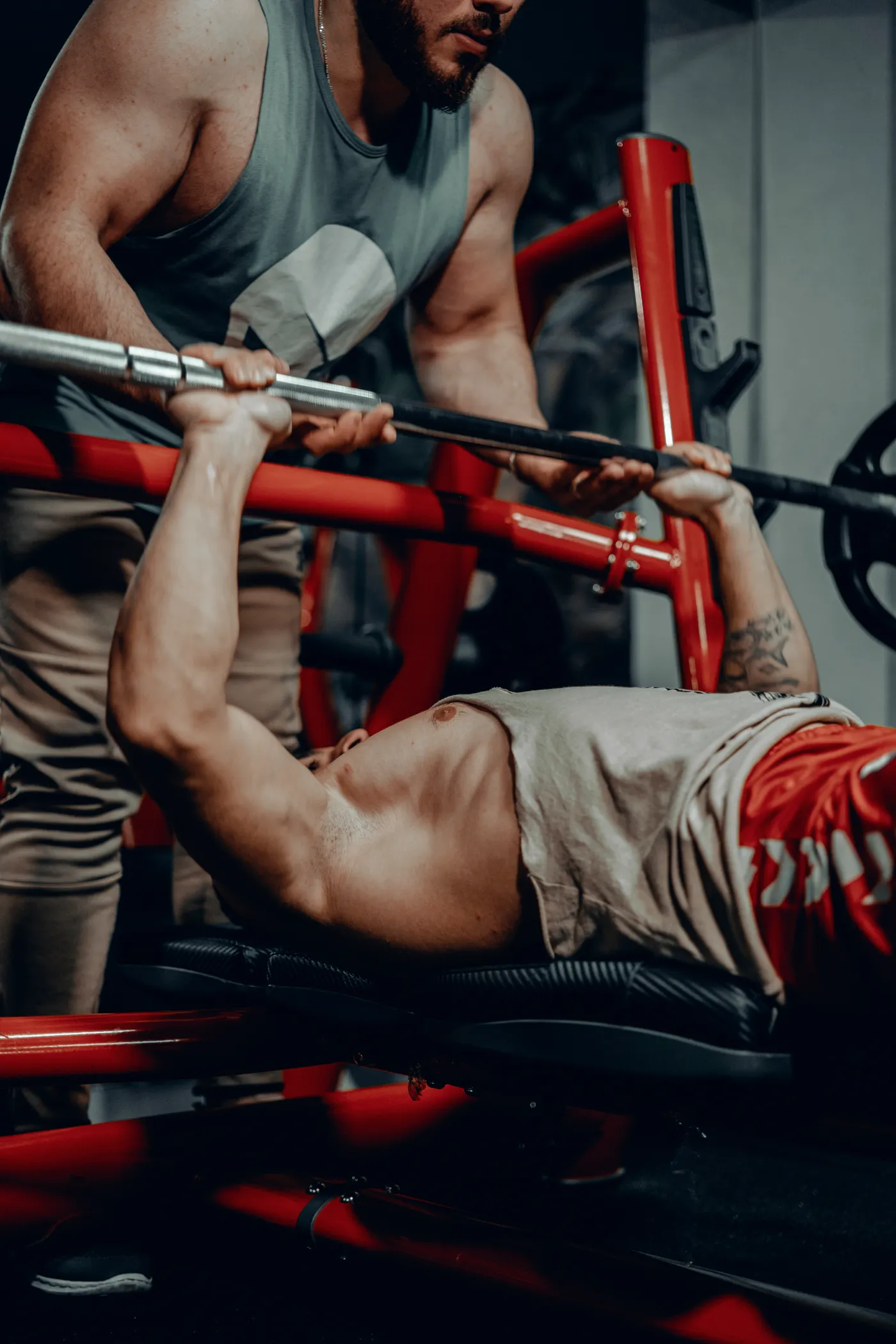 Man bench pressing under a trainer's supervision in a gym