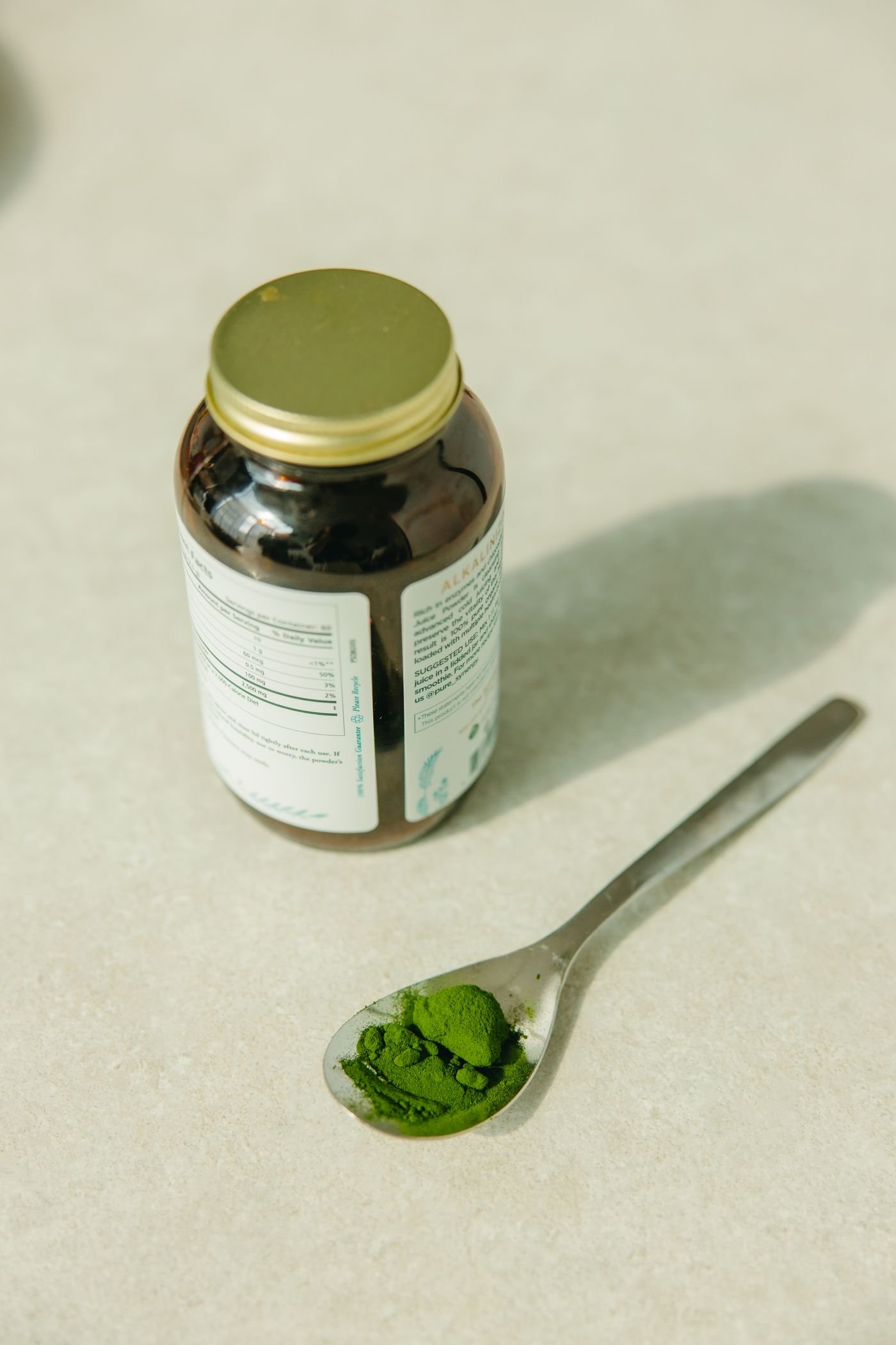 Spoon of green nutritional powder beside a jar, illustrating supplement labeling rather than creatine itself