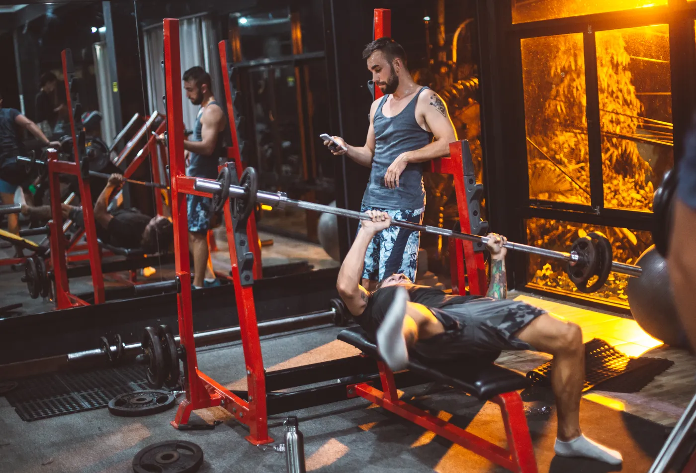 Trainer checking a phone beside a lifter bench pressing