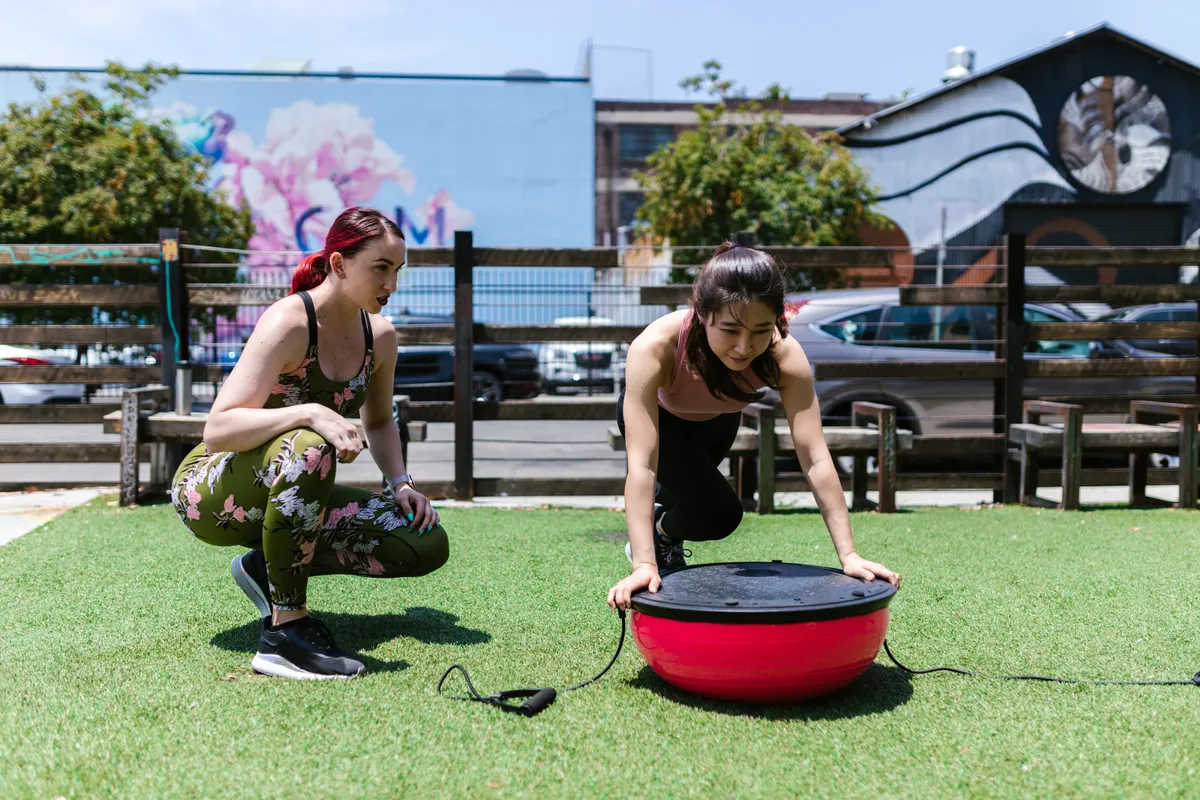 Trainer supervising an athlete using a red balance platform outdoors