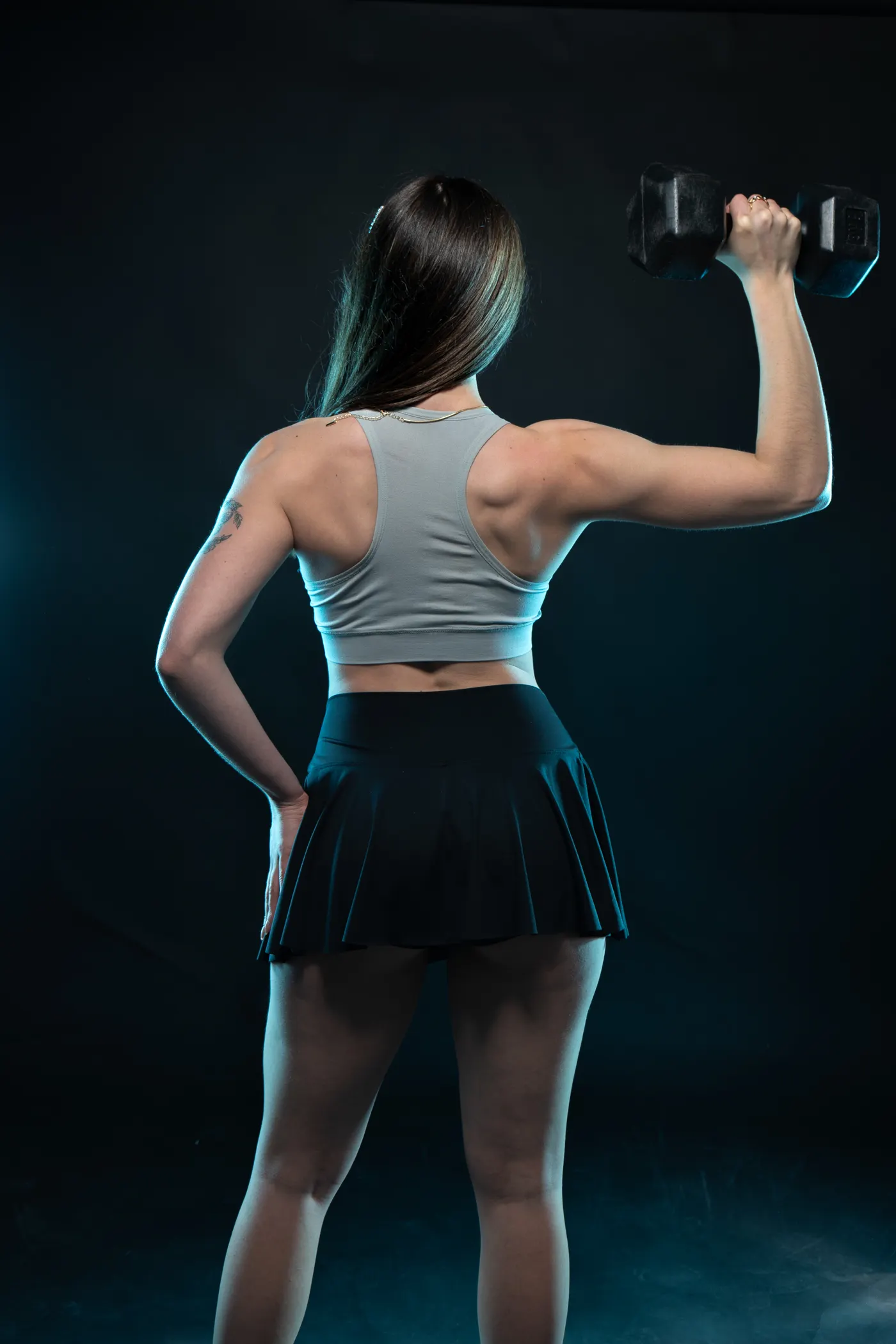 Back view of a strong woman holding a dumbbell in a gym