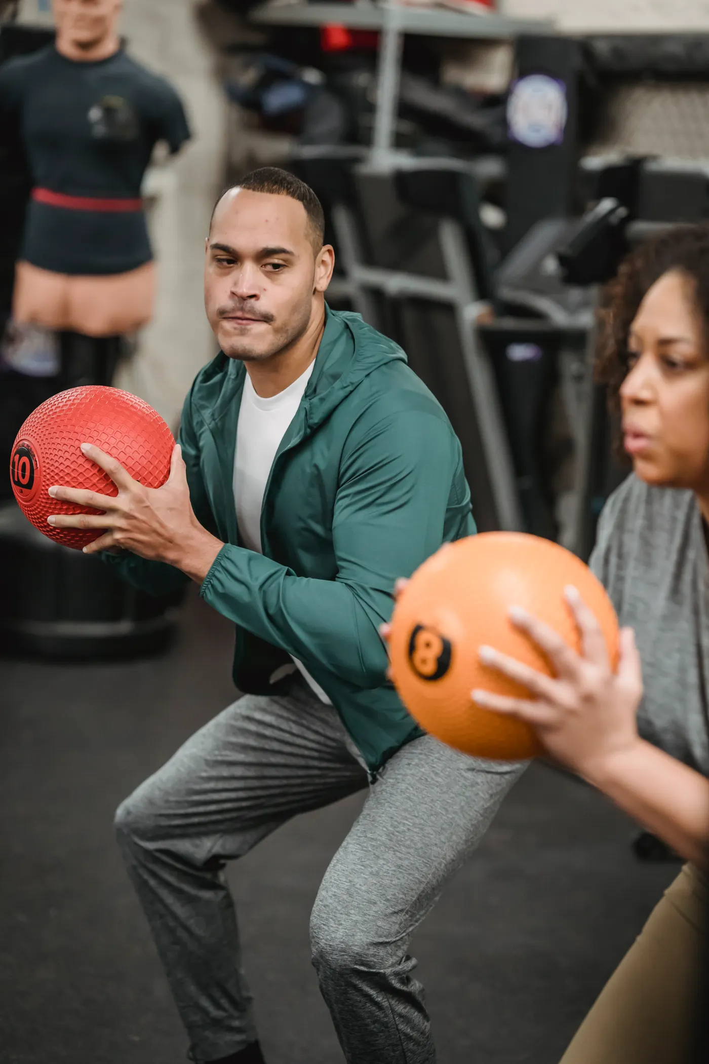 Trainer and athlete practicing medicine-ball squats in a gym