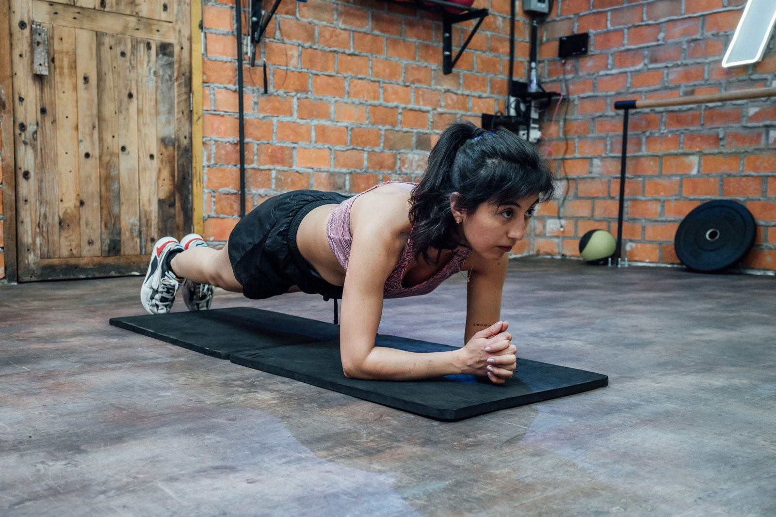 Woman holding a forearm plank on a mat in a brick-walled gym