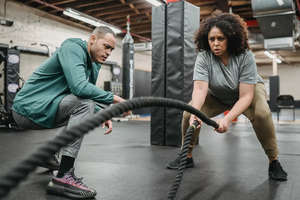 Woman training with battle ropes under a coach's supervision