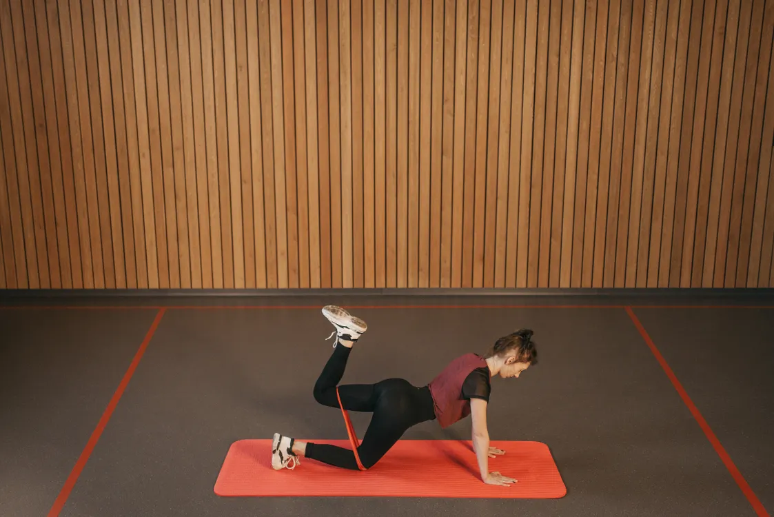 Woman performing a resistance-band exercise on an indoor workout mat