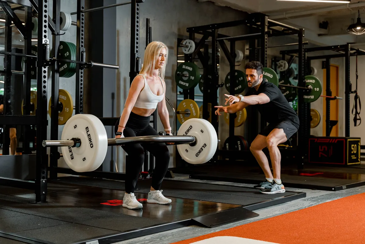 Woman lifting a barbell on stable ground under a coach's supervision