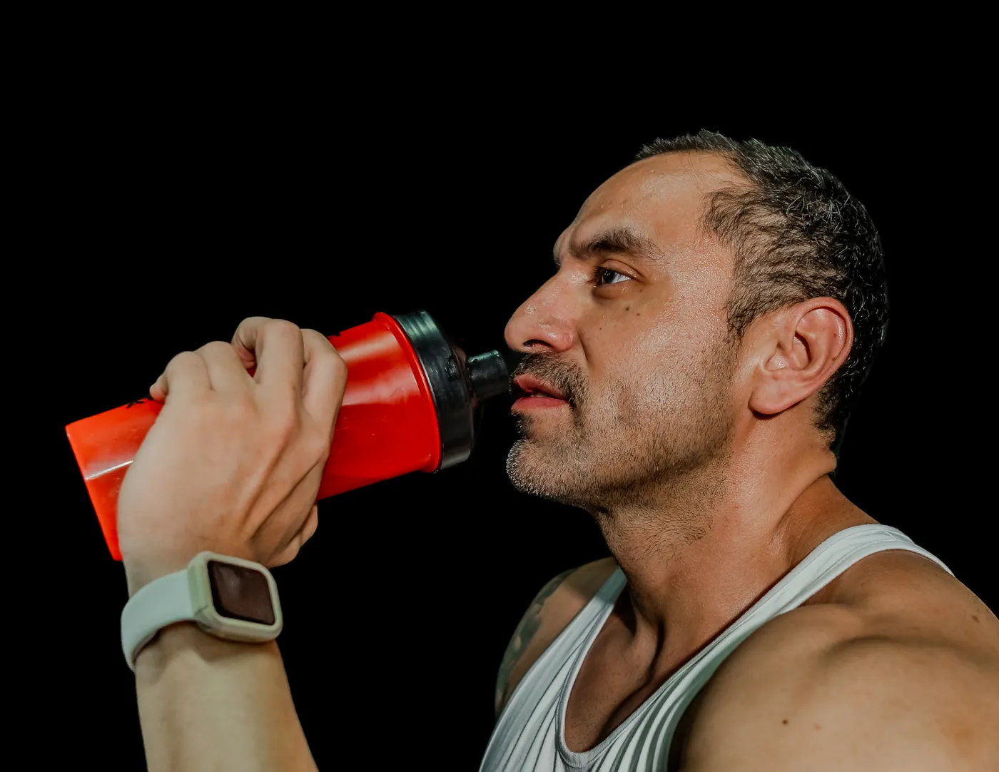 Athlete drinking from a shaker bottle against a dark studio background