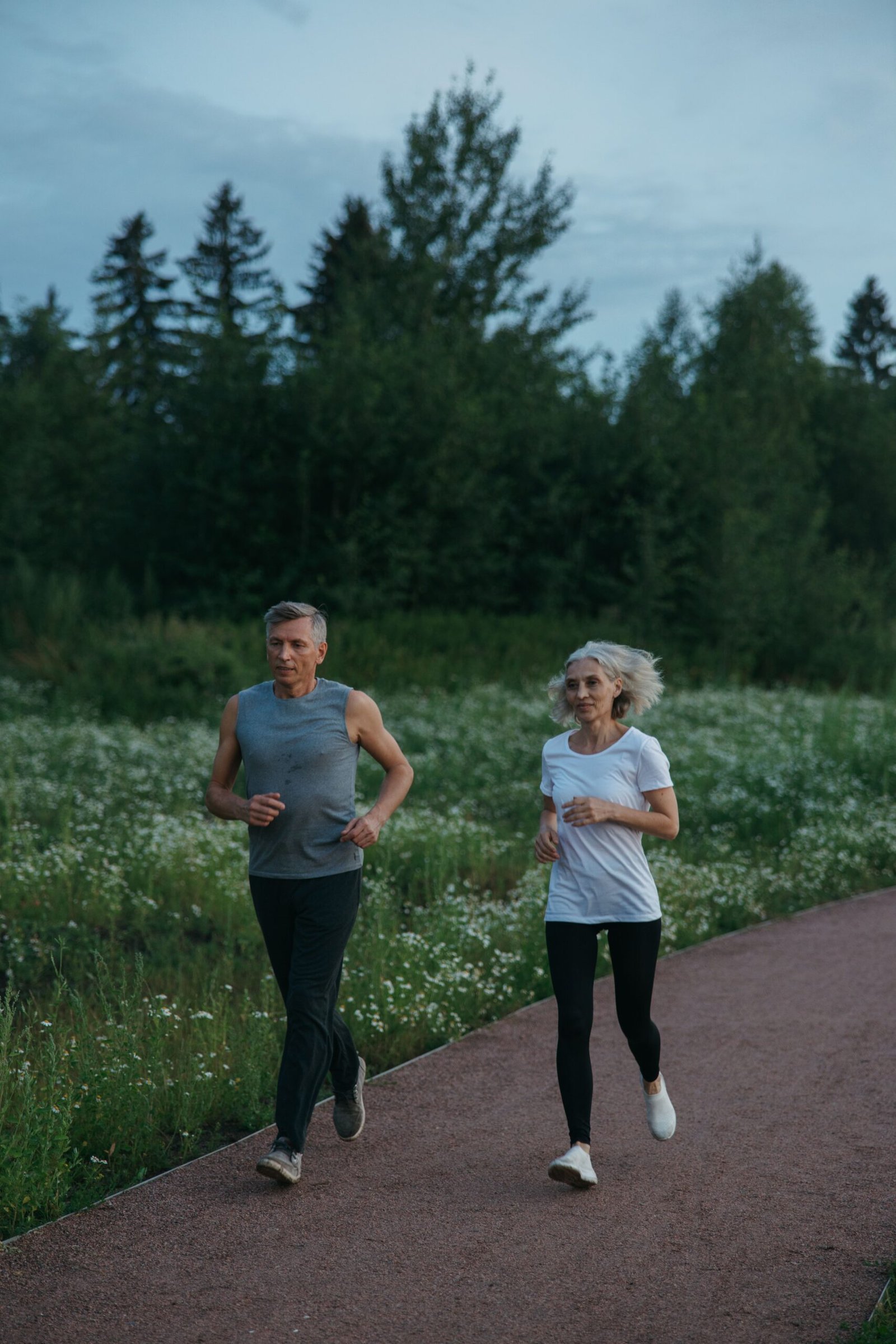 Older couple jogging together along a wooded park trail