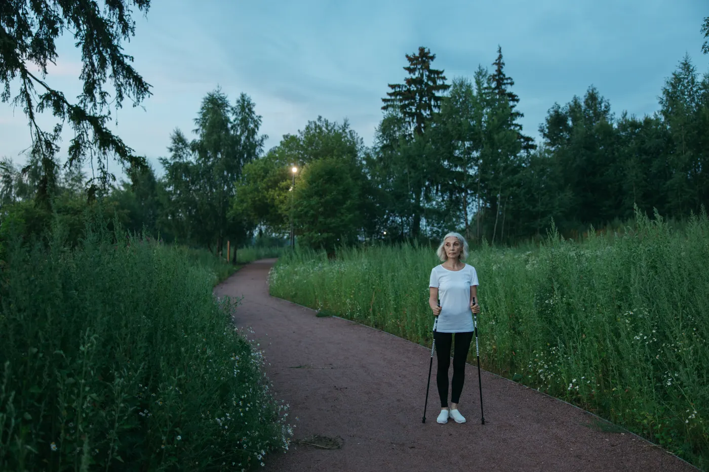 Senior woman using Nordic walking poles on a park path