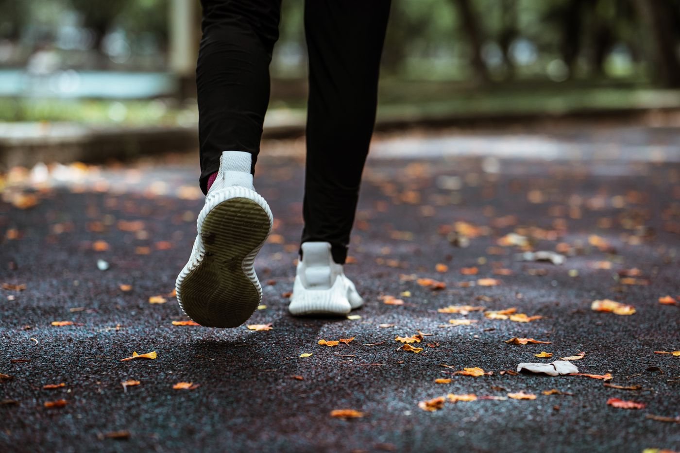 Close-up of running shoes on a leaf-covered park path