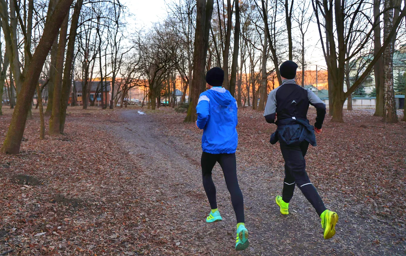 Two runners jogging along a leaf-covered park trail