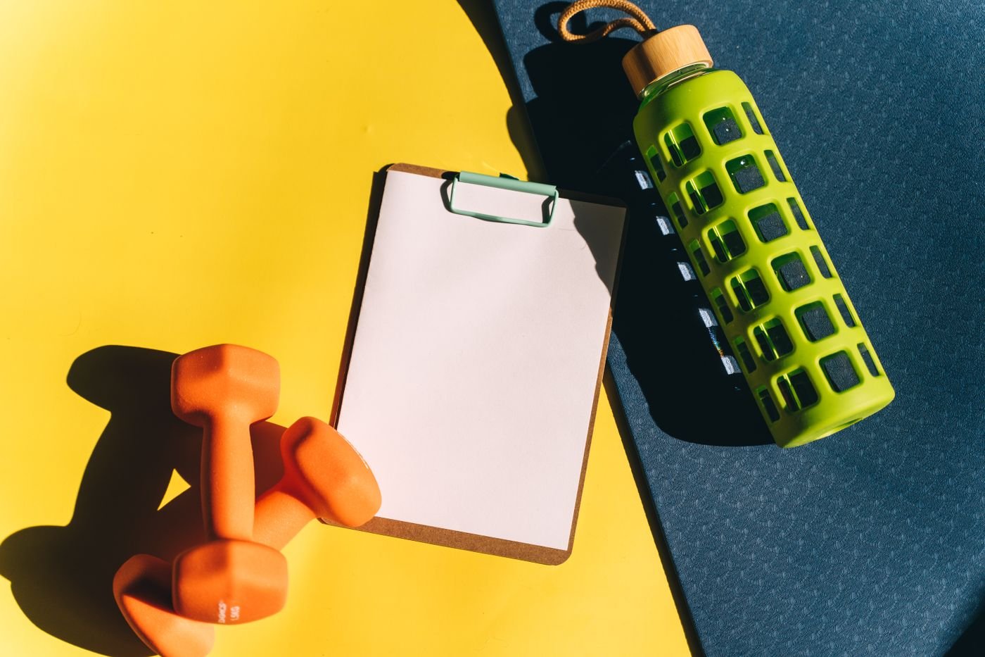 Workout planning clipboard and dumbbells on a bright background