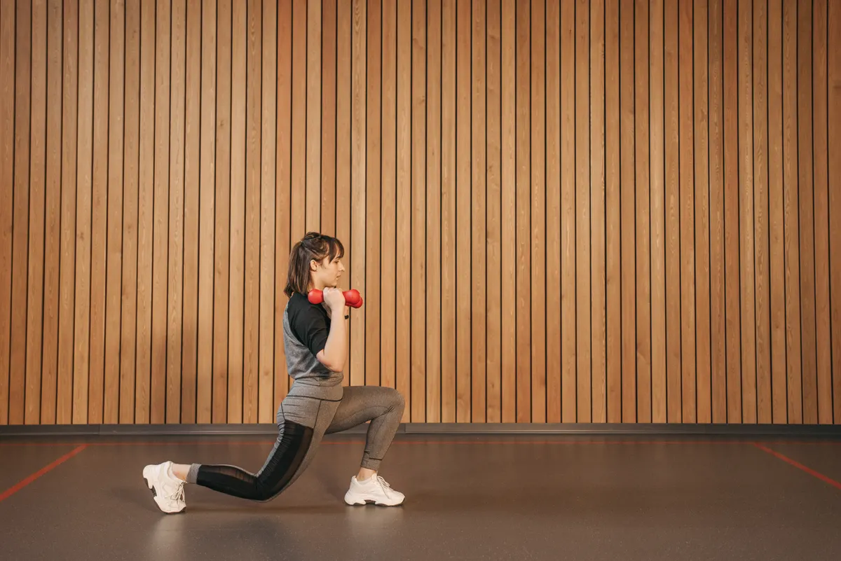 Woman performing a controlled lunge with dumbbells in a training studio