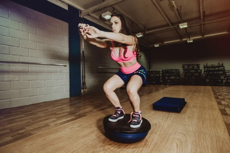 Woman performing a controlled squat on a BOSU balance trainer in a gym