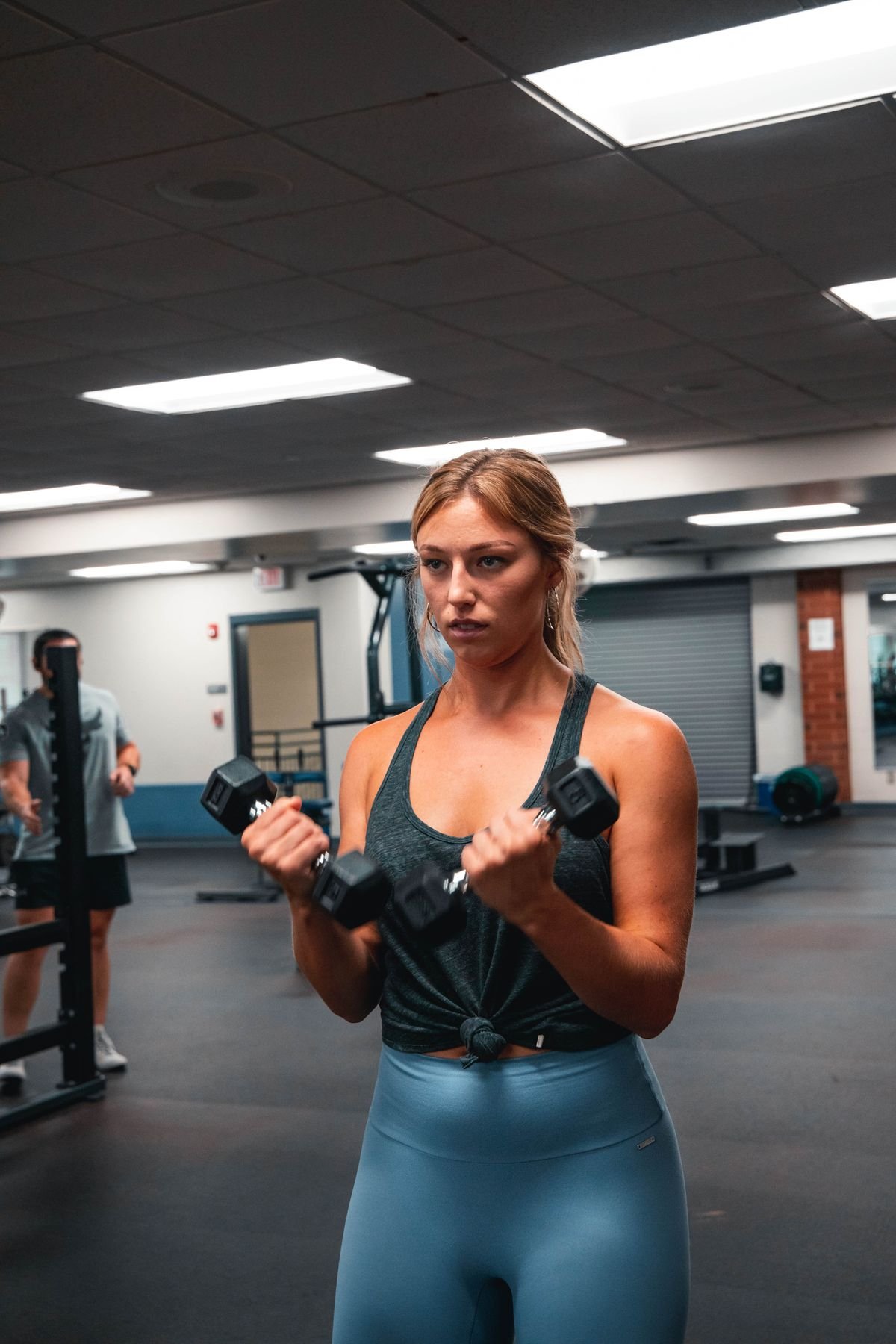 Woman performing standing dumbbell curls in a gym