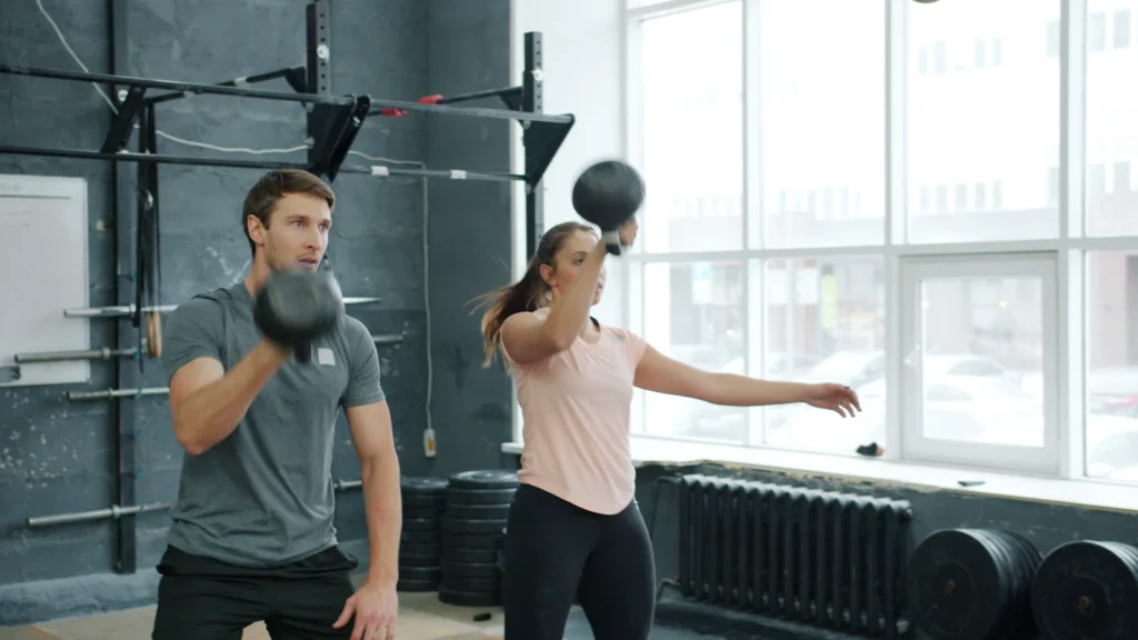 Two athletes training with kettlebells in a gym