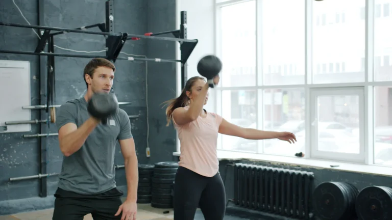 Two athletes training with kettlebells in a gym