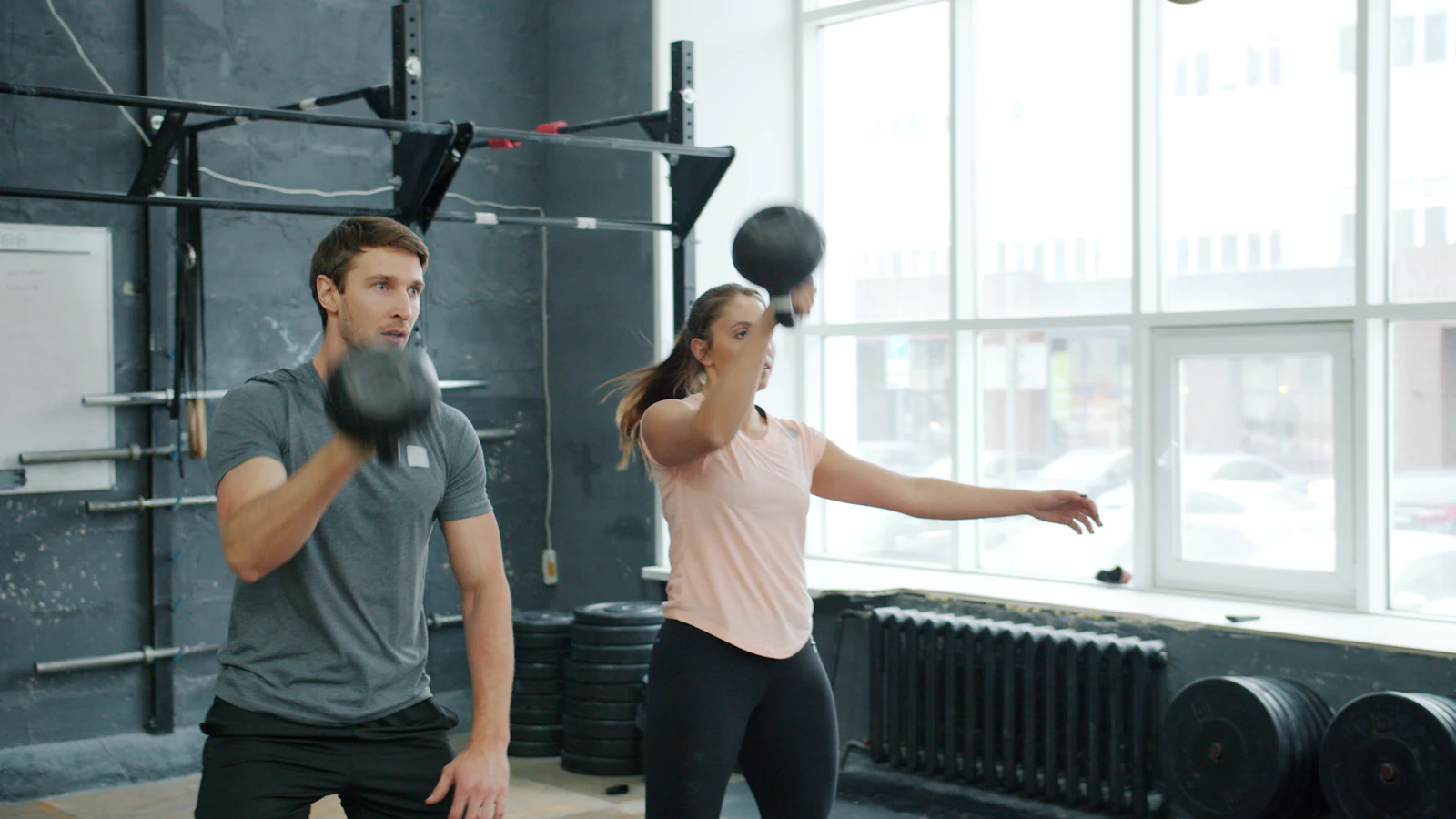 Two athletes training with kettlebells in a gym