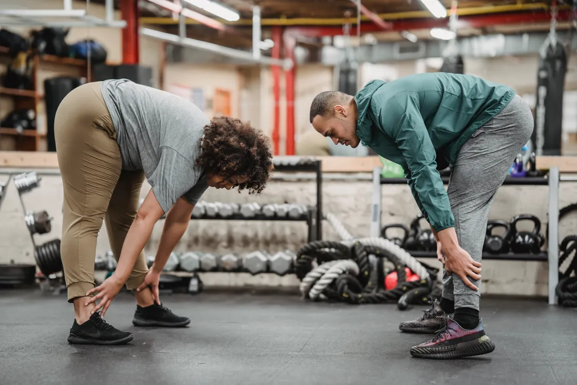 Two adults reaching toward their feet in a gym