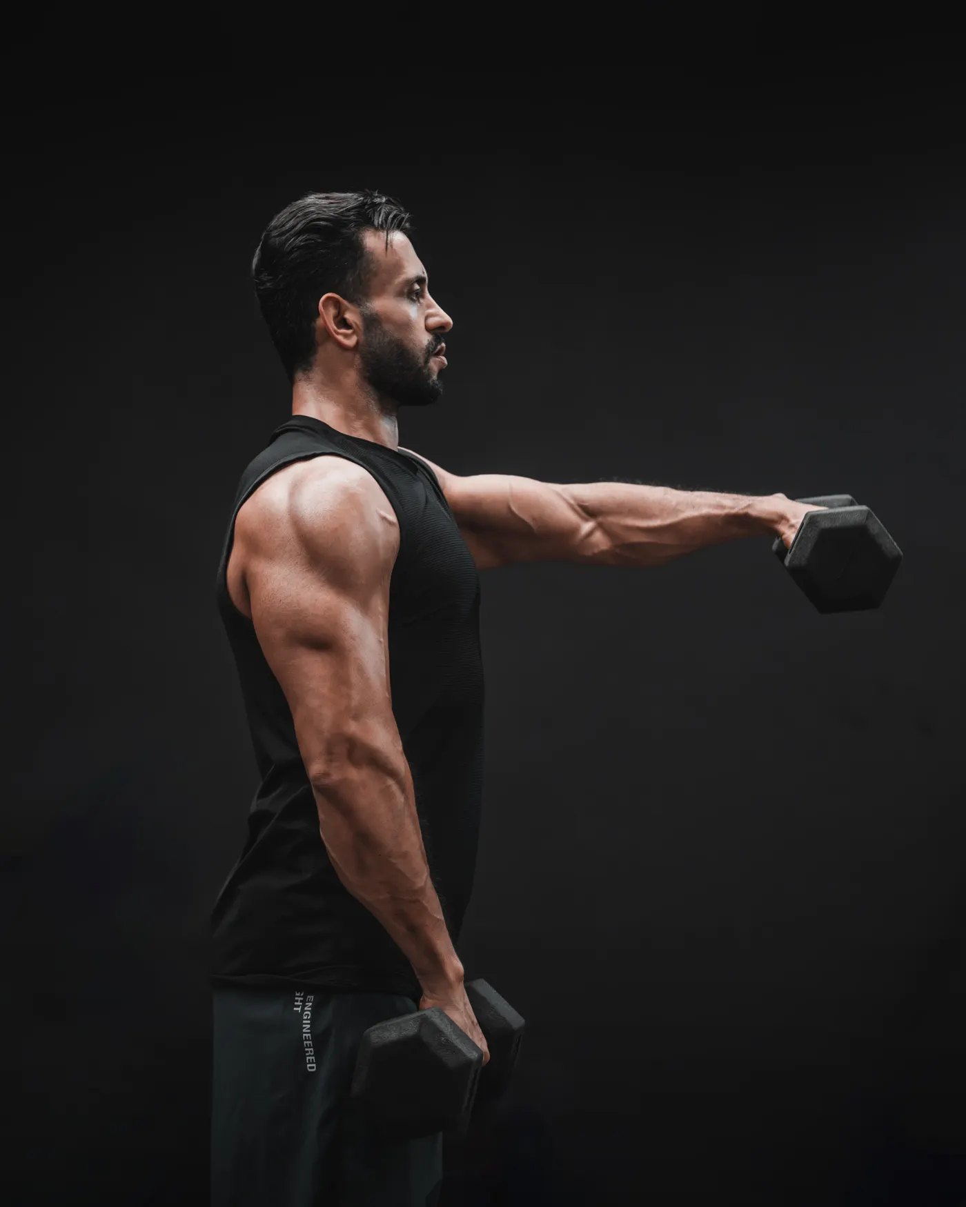 Muscular man performing dumbbell side raises in a gym