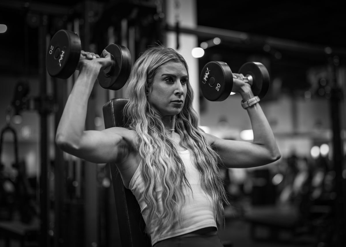 Woman performing a dumbbell exercise on a gym bench