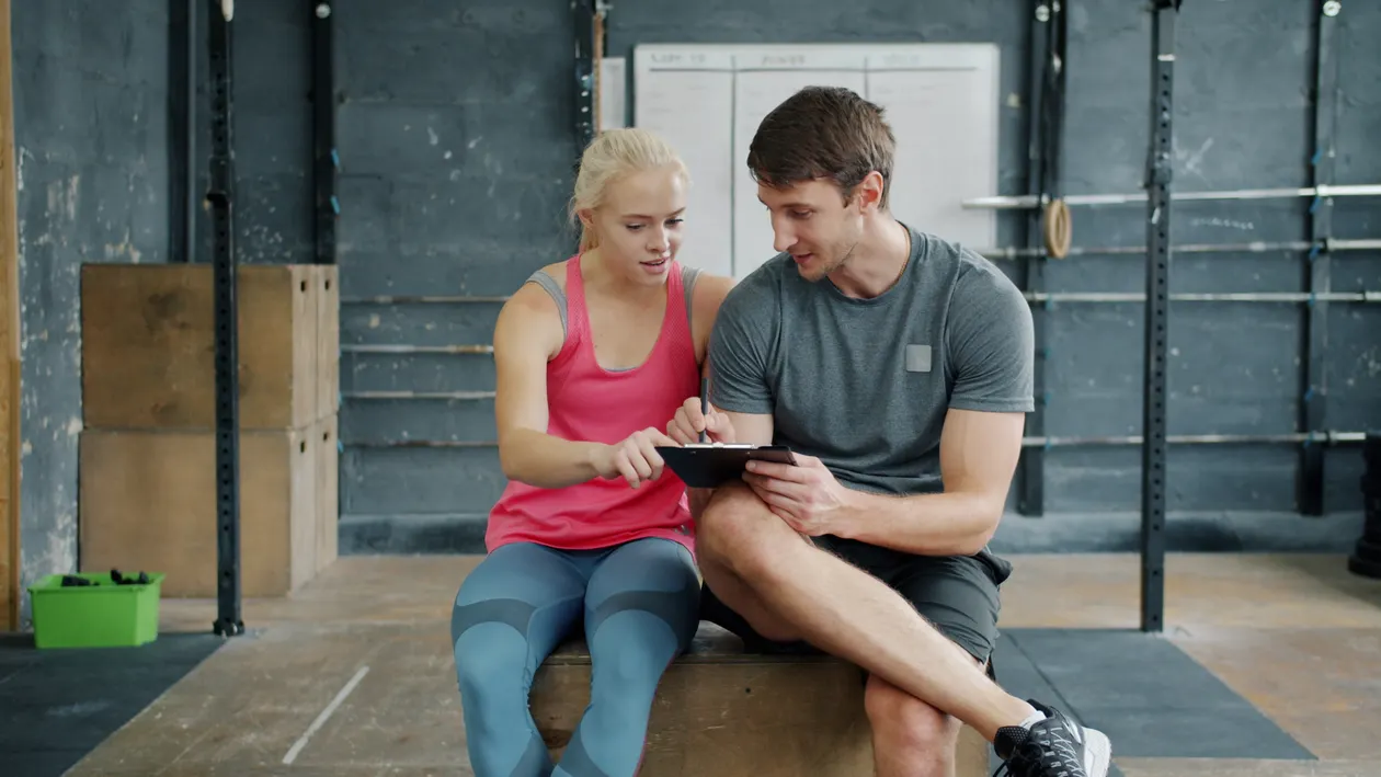 Two gym-goers reviewing a strength-training plan on a tablet